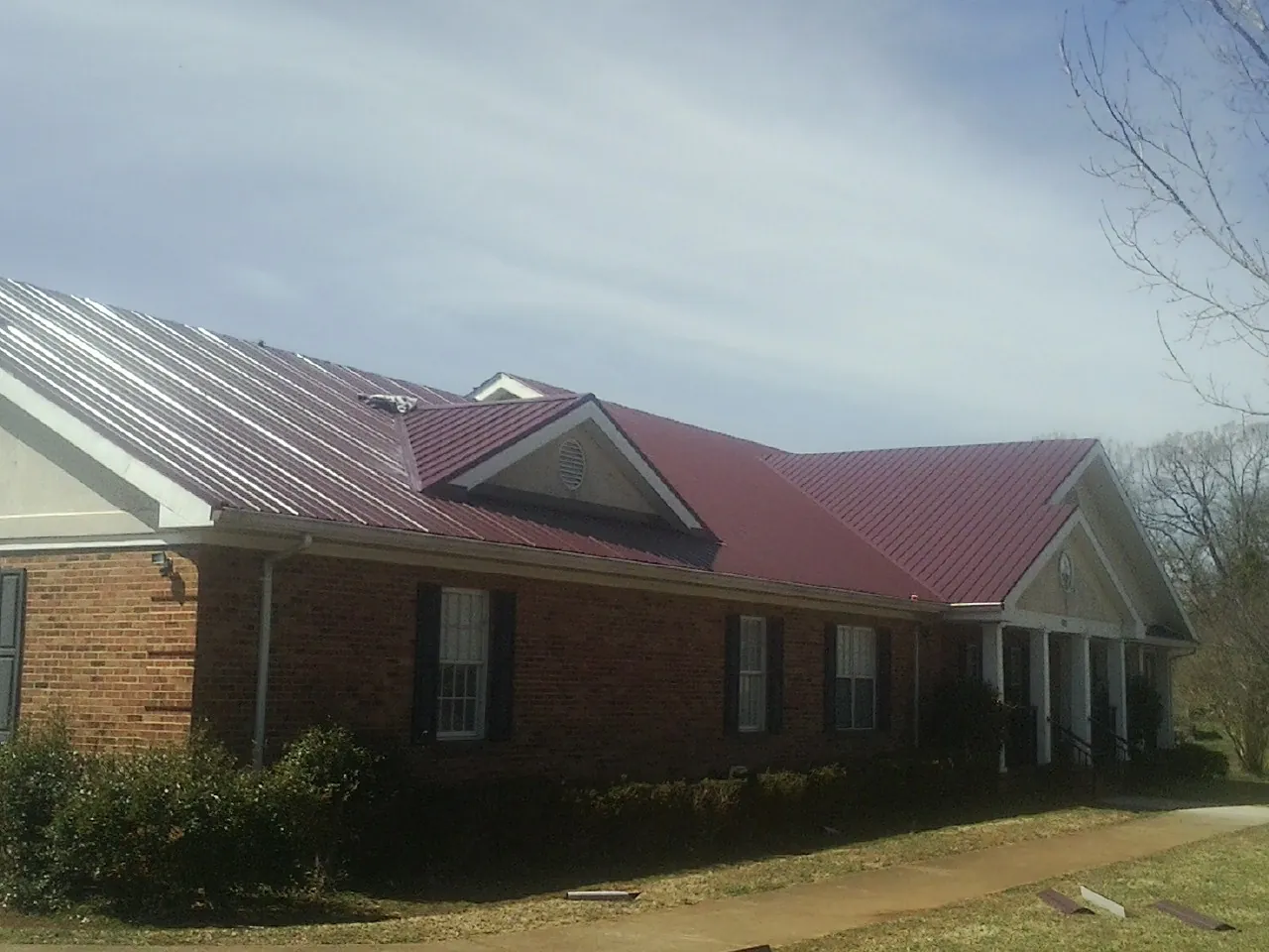 Red metal roof with gabled entries on a long brick building, from a Hail Damage Roof Repair job in Jordan