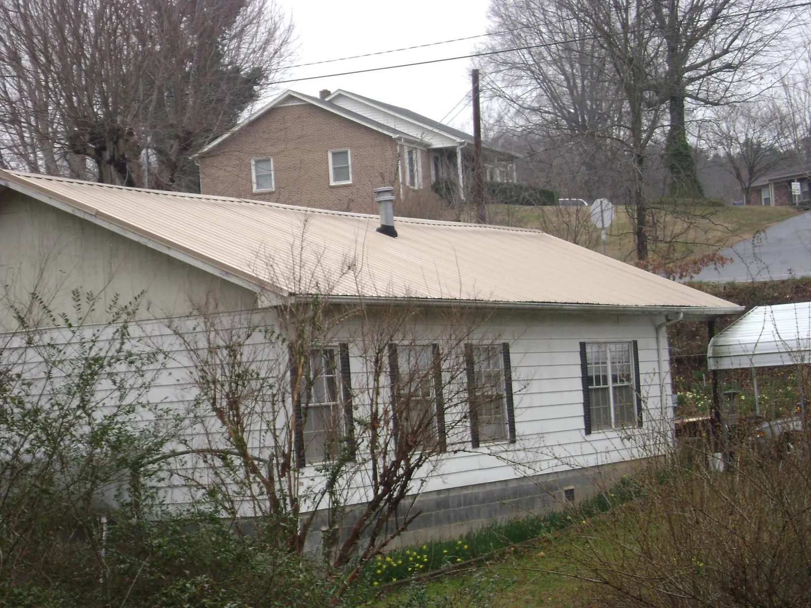 Tan metal roof on a white sided house set into a hillside — Commercial Roofing by Roofing Brothers in Jordan