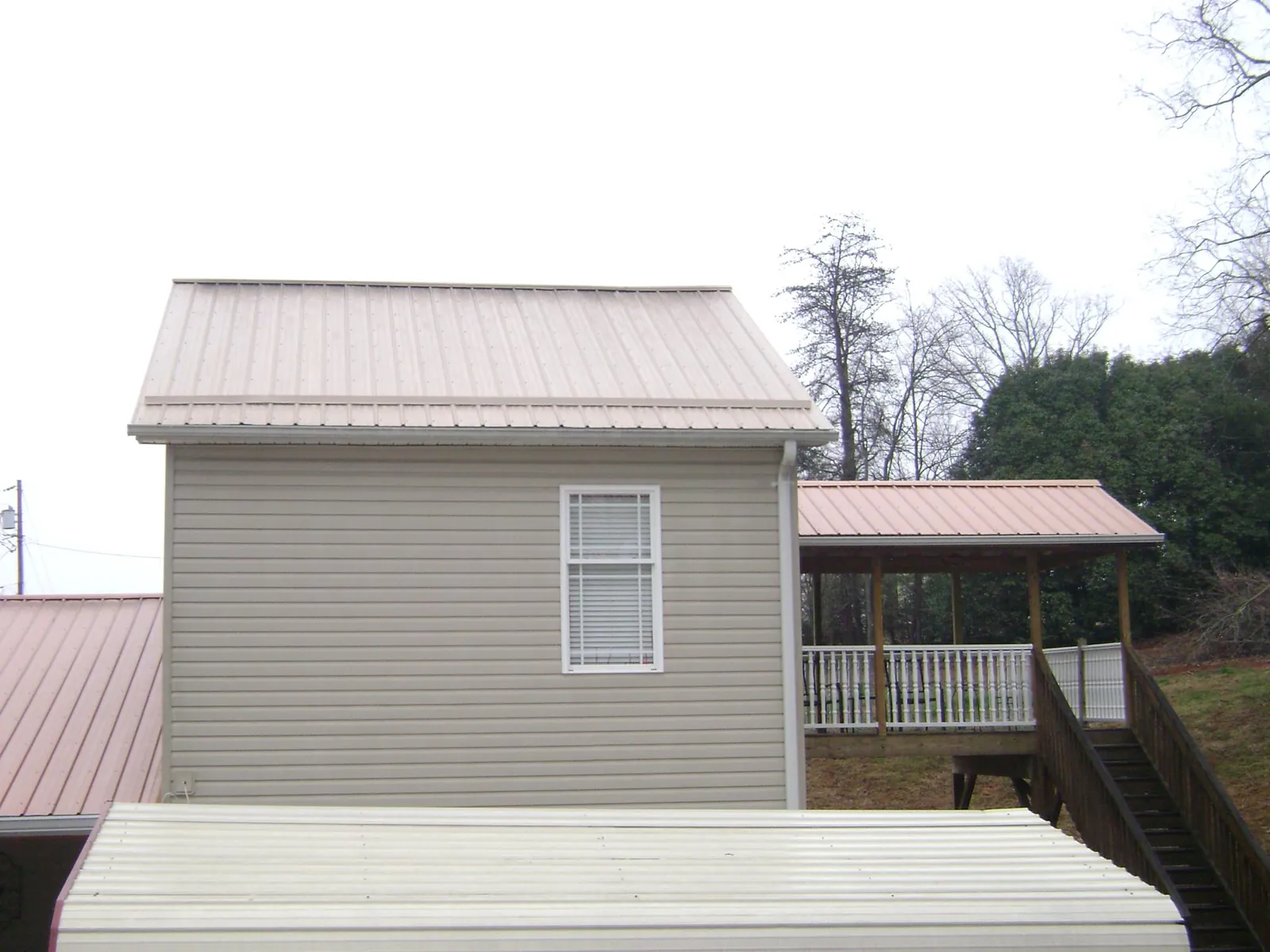 Tan metal roofs on a two story addition and attached porch, from a Roof Replacement job in Jordan